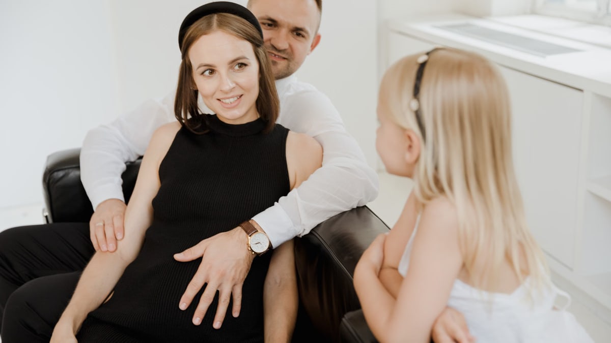 A pregnant woman sits with her family on a sofa, capturing a warm moment of togetherness.