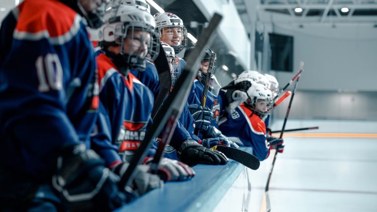 A youth ice hockey team wearing blue jerseys and helmets stands ready on the rink.