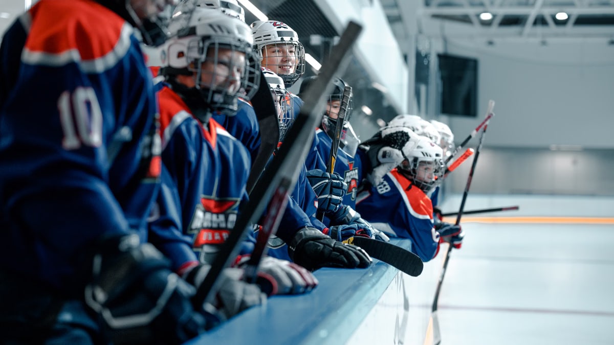 A youth ice hockey team wearing blue jerseys and helmets stands ready on the rink.
